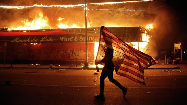 Протестующий несет перевернутый американский флаг возле горящего здания в Миннеаполисе